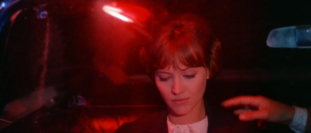 Pierrot Le Fou (Crazy Pete) (1965) movie still: closeup — A dark vehicle interior is filled with harsh red light. A young woman sits while a hand…
