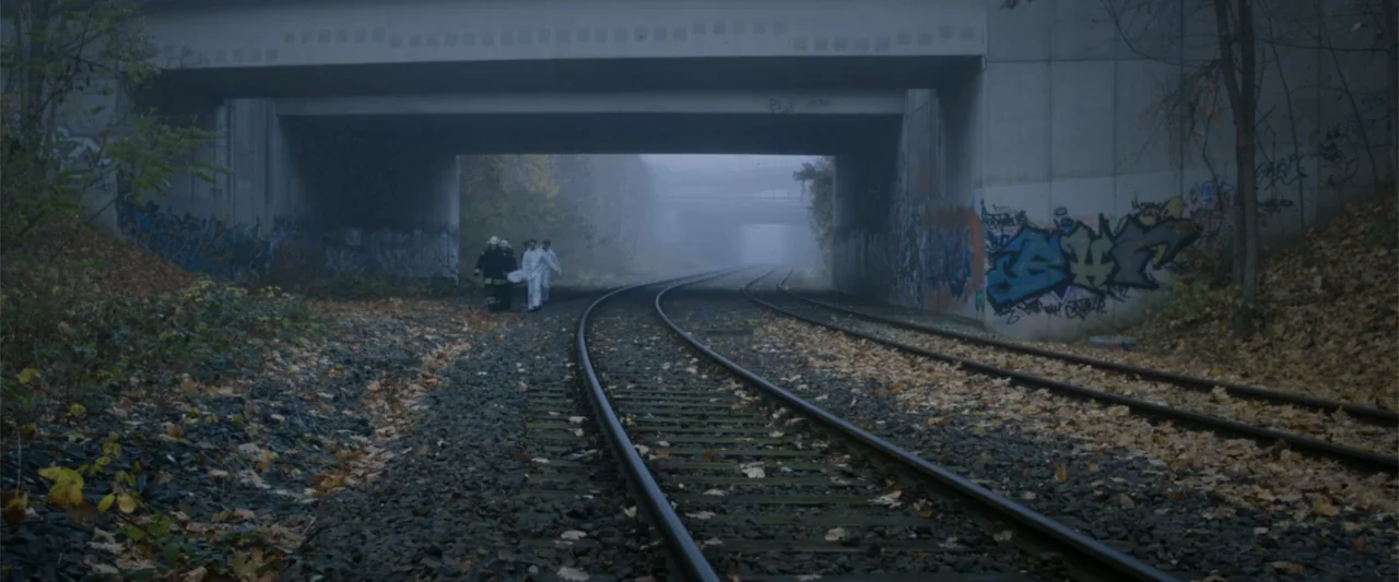 Heartburn (1986) movie still: wide — A concrete railway underpass is covered in graffiti and surrounded by fallen autumn leaves. Three individuals…
