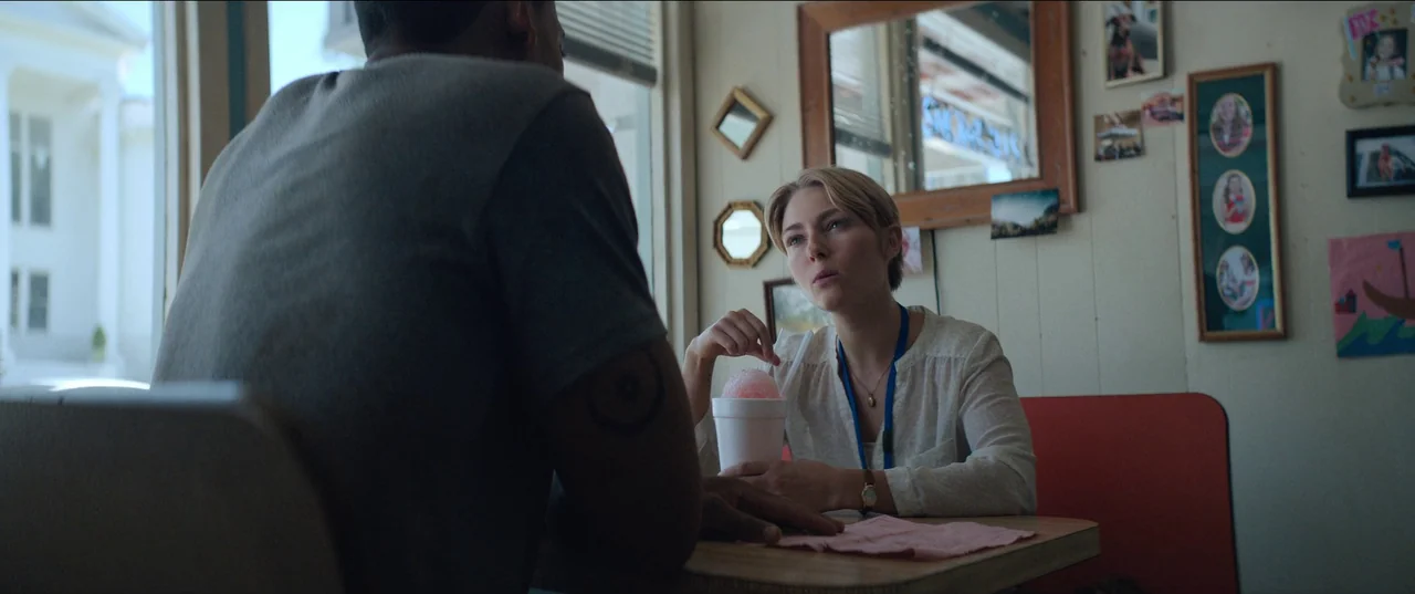Rebel Ridge (2024) movie still: medium — A booth in a vintage-style establishment features wood-paneled walls decorated with multiple framed photos.…