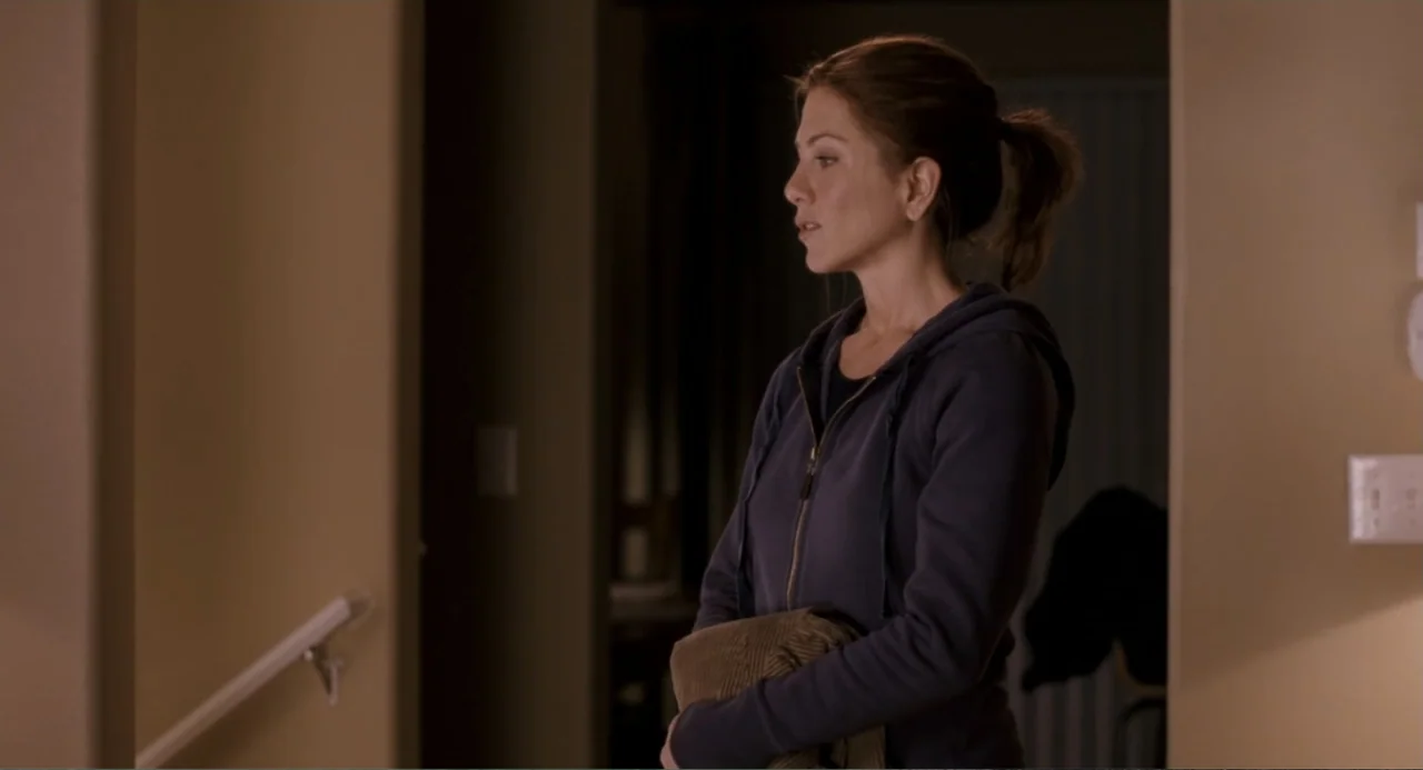 Management (2009) movie still: medium — A residential hallway features beige walls and a light switch plate. A woman in a dark hoodie stands holding…