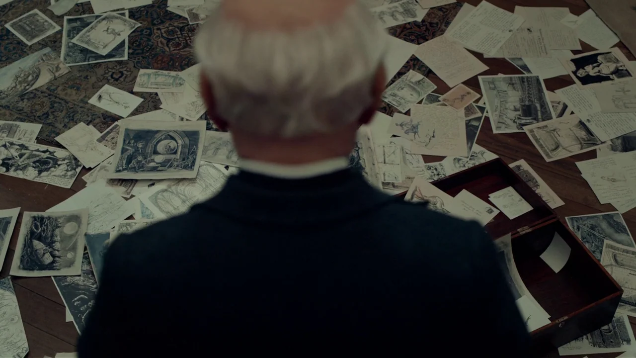 Hugo (2011) movie still: medium — A floor is covered in a dense arrangement of scattered paper drawings and notes. A man stands at the edge of the…