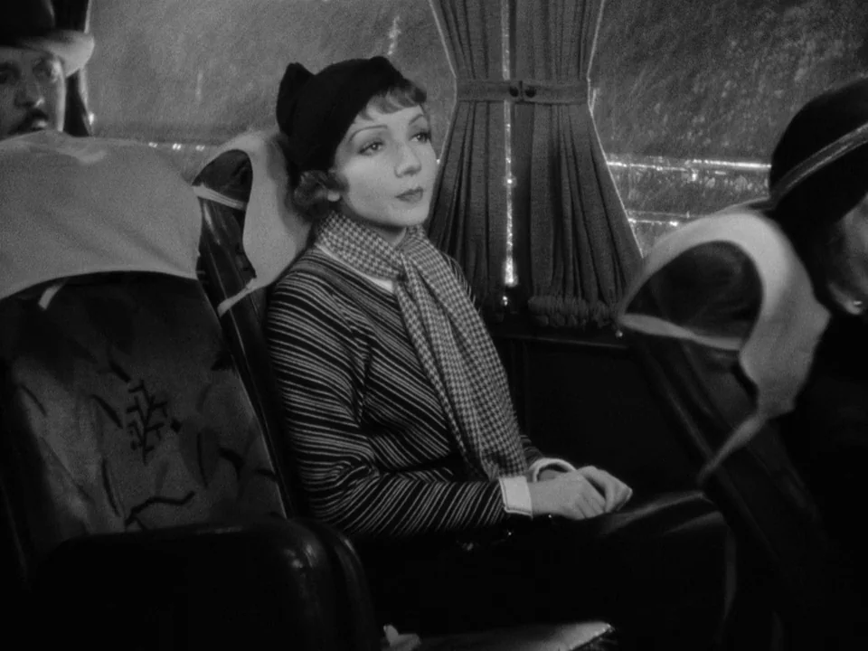 It Happened One Night (1934) movie still: medium — Interior of a vintage passenger bus at night with patterned seats and pleated curtains. A woman…