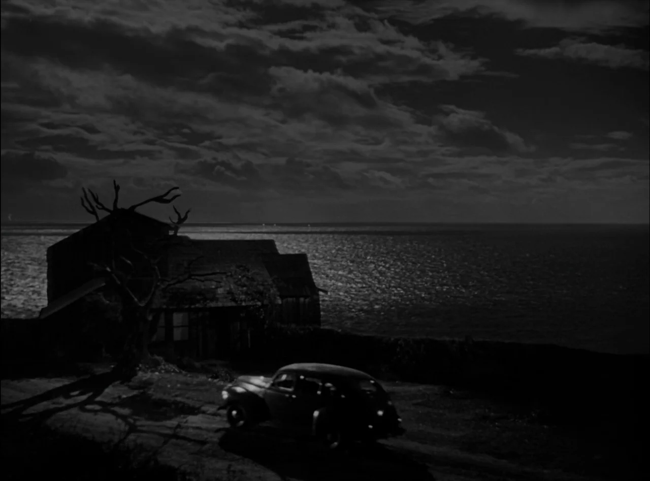 Criss Cross (1949) movie still: wide — A house sits on a cliff overlooking a dark ocean under a cloudy sky. A vintage car is parked on the dirt…