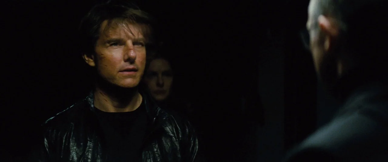 Mission: Impossible – Rogue Nation (2015) movie still: medium — A man stands in a poorly lit space with another figure partially visible in…