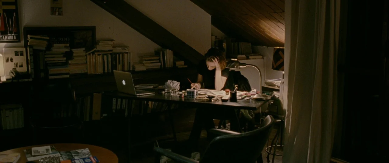 Personal Shopper (2016) movie still: wide — An attic workspace features low sloping wooden ceilings and walls lined with many books. A young woman…