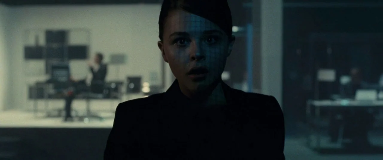 Clouds of Sils Maria (2014) movie still: closeup — A dark, modern professional workspace with blurred workstations and desk lamps in the background.…