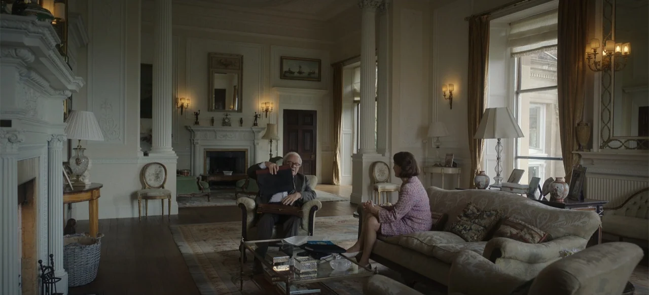 One Life (2023) movie still: wide — A formal, high-ceilinged drawing room features ornate moldings, tall white columns, and period furniture. An…