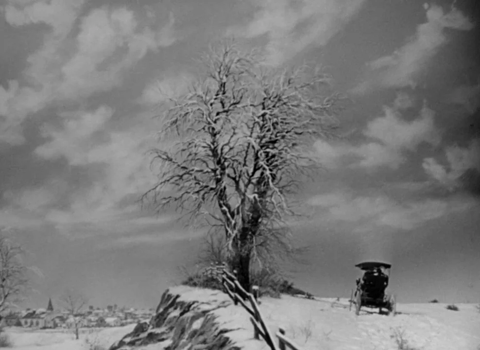 The Magnificent Ambersons (1942) movie still: wide — A snow-covered hill features a large leafless tree in the foreground. In the distance, a…