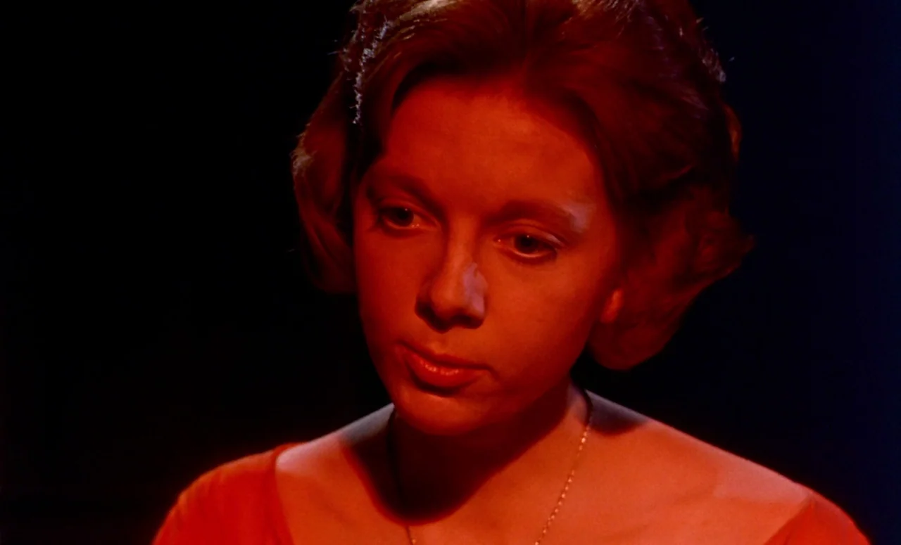 Peeping Tom (1960) movie still: closeup — A woman's face is illuminated in a dark room against an absolute black background. The subject is wearing…