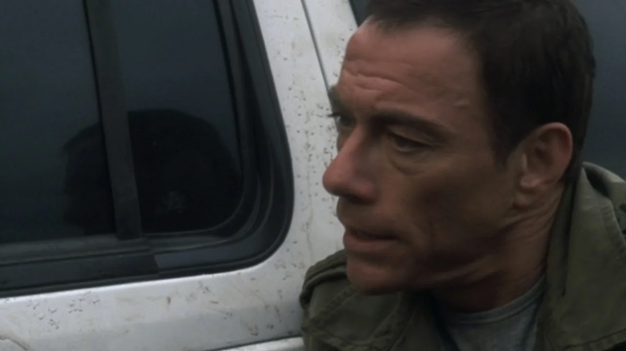 The Shepherd (2023) movie still: closeup — A man stands outdoors next to the window of a white dirty vehicle. The man gazes off-camera while leaning…