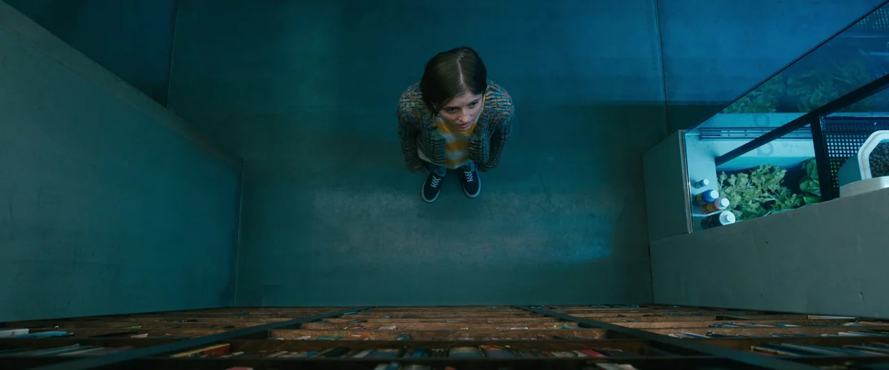 Leave The World Behind (2023) movie still: wide — A spacious room features a large bookshelf spanning the width of the floor. A woman stands in the…
