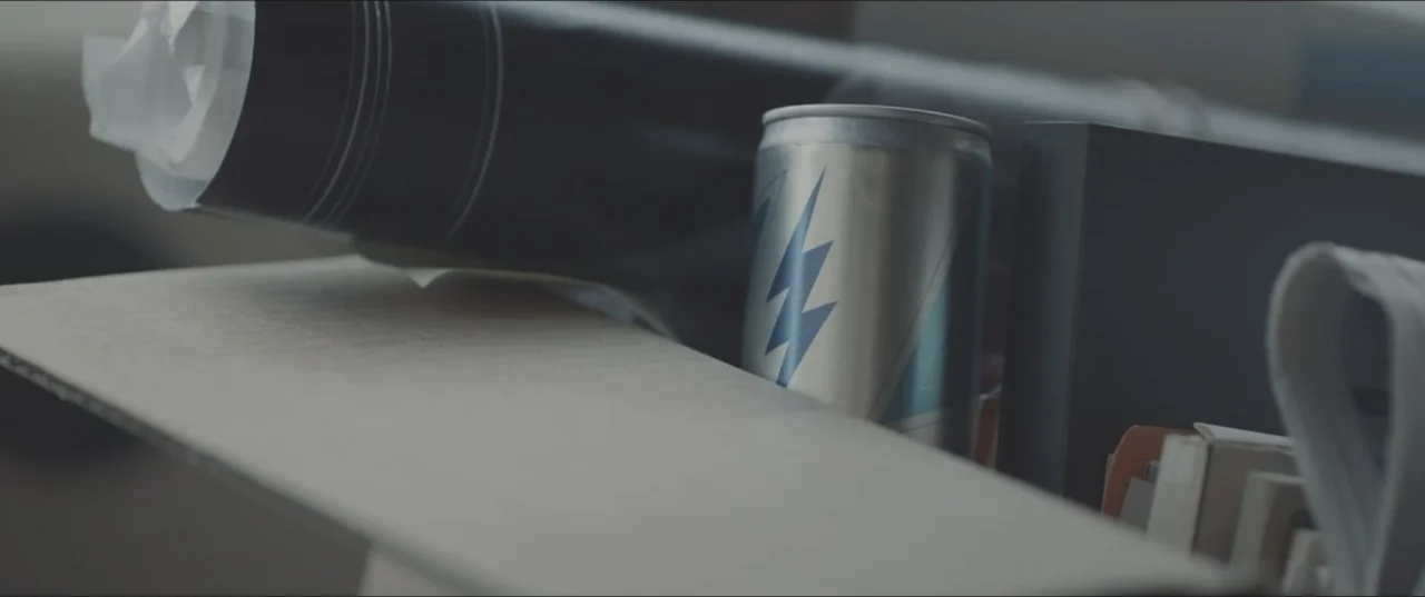 Zoe (2018) movie still: closeup — A collection of items rests within an open cardboard box in a dim room. A silver energy drink can with a blue…