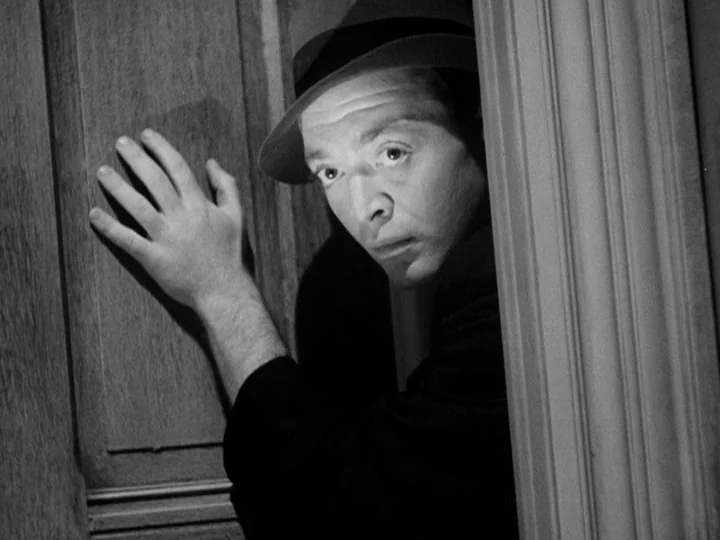 Stranger on the Third Floor (1940) movie still: closeup — A dark wooden door frame separates the man from the adjacent dimly lit space. The man…