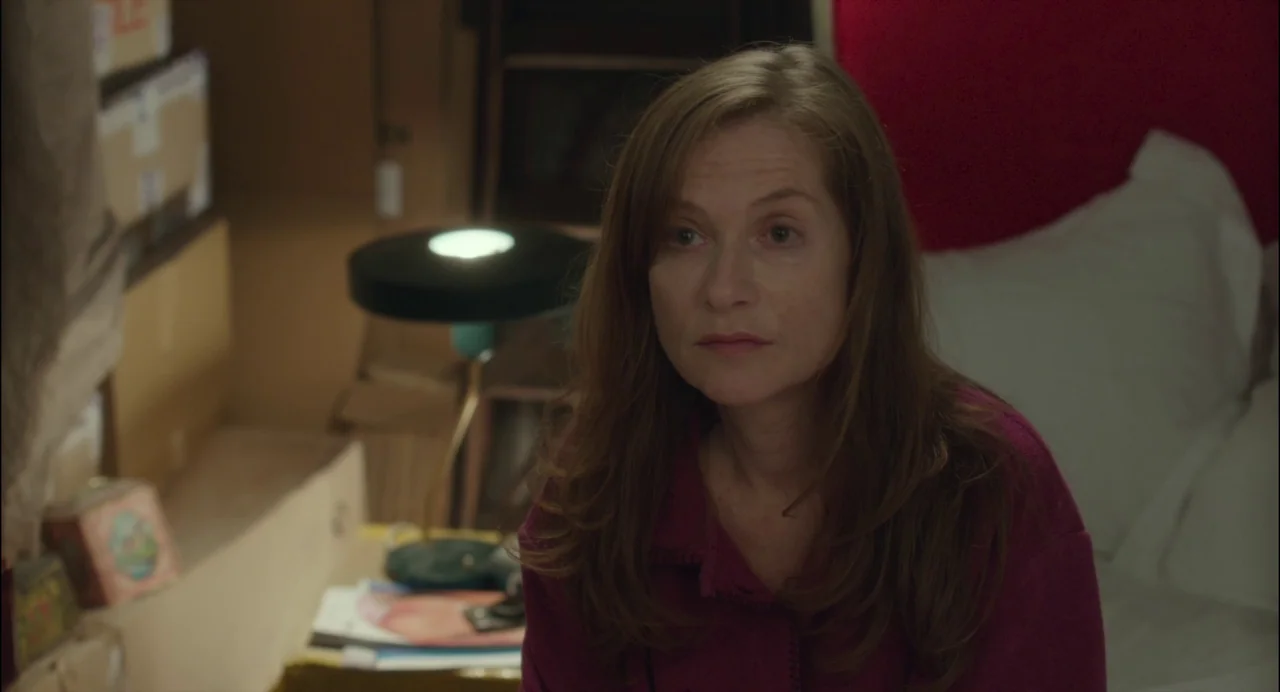 Abuse of Weakness (2013) movie still: medium — A cluttered interior space with stacked boxes and a table lamp behind a person. The woman with auburn…