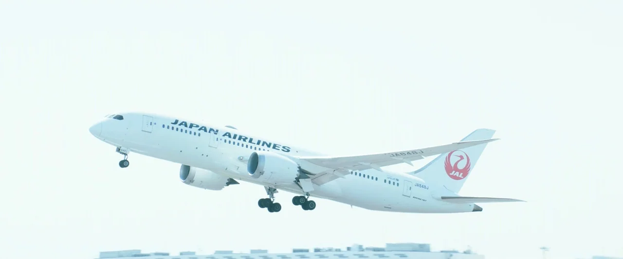 Angel Flight THE MOVIE (2026) movie still: wide — A white Japan Airlines passenger jet ascends into a bright, washed-out sky. The aircraft climbs…