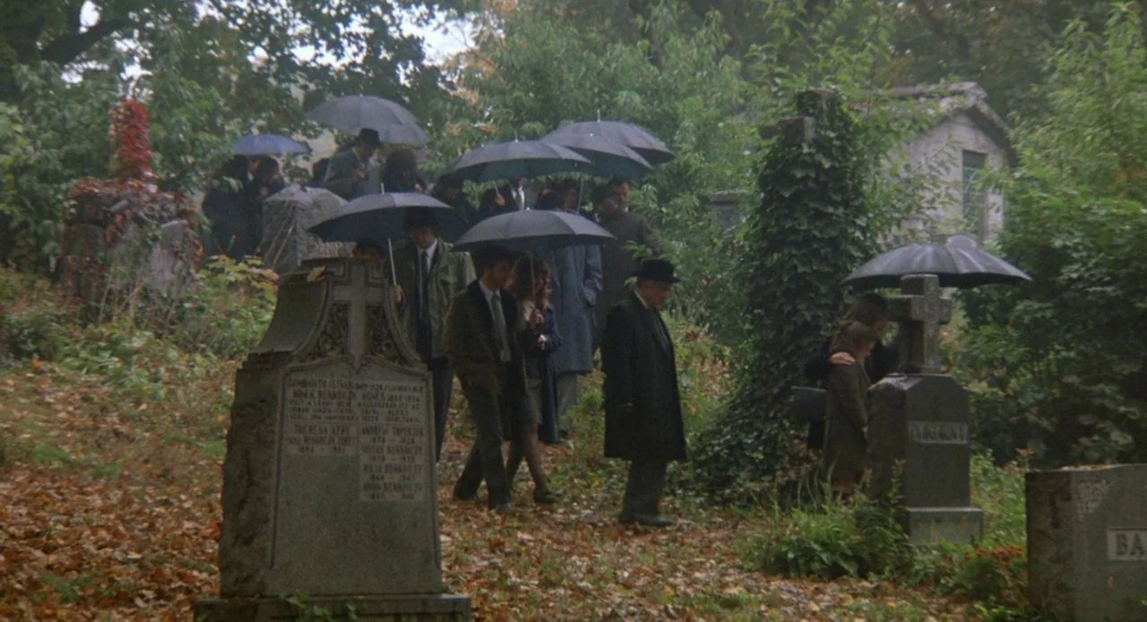 Jacob’s Ladder (1990) movie still: wide — A group of mourners walks through an overgrown cemetery filled with old stone monuments. The people carry…