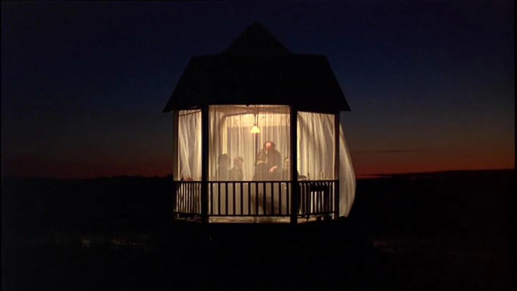Days Of Heaven (1978) movie still: wide — A wooden gazebo stands illuminated in the dark landscape against a sunset horizon. Four individuals are…