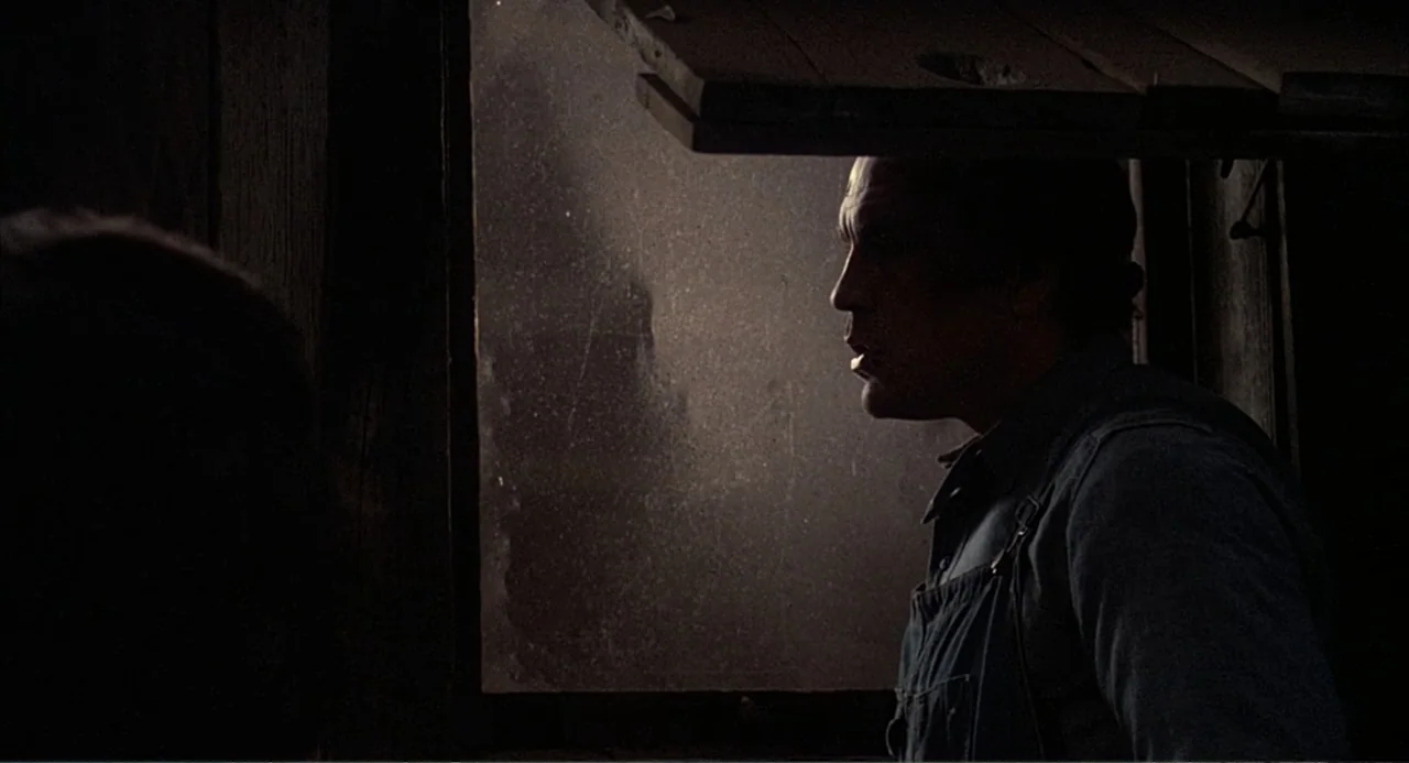 Of Mice and Men (1992) movie still: medium — A dark wooden barn interior with a single window letting in dusty light. A middle-aged man in denim…