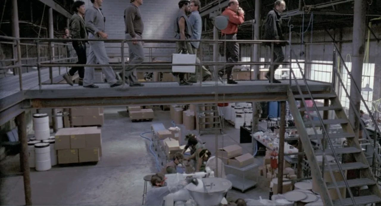 RoboCop (2014) movie still: wide — A wide industrial warehouse features a steel catwalk overlooking the lower assembly floor area. Multiple workers…