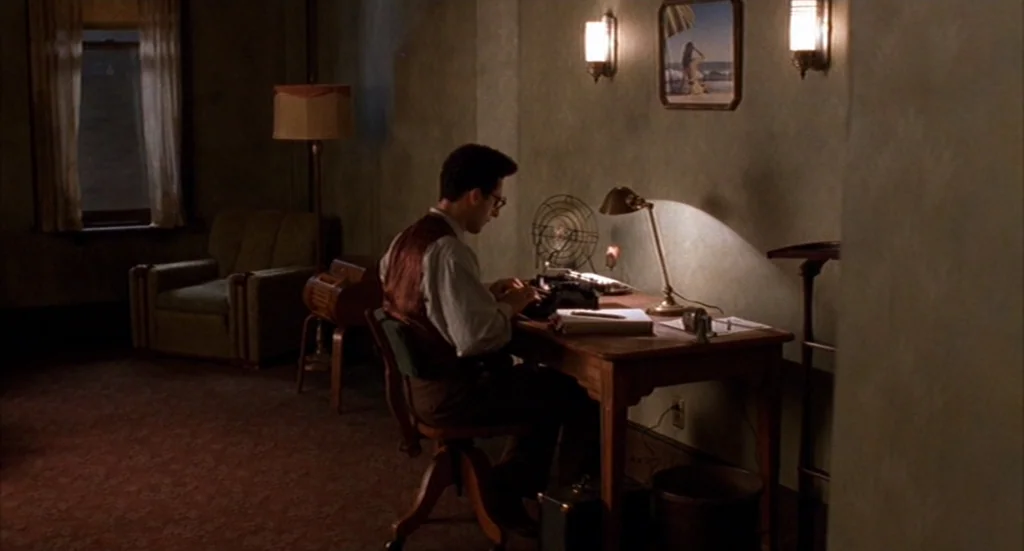 Barton Fink (1991) movie still: medium — A dimly lit room with vintage furniture and a dark patterned carpet. A man sits at a wooden desk typing on…