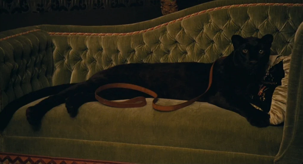 House of Tolerance (2011) movie still: medium — A velvet green sofa features tufted upholstery and a decorative trim along the bottom edge. A black…