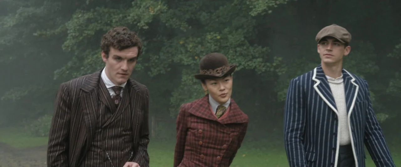 Young Sherlock Holmes (1985) movie still: medium — Three people stand before a dense patch of trees on an overcast day. They stand side-by-side…