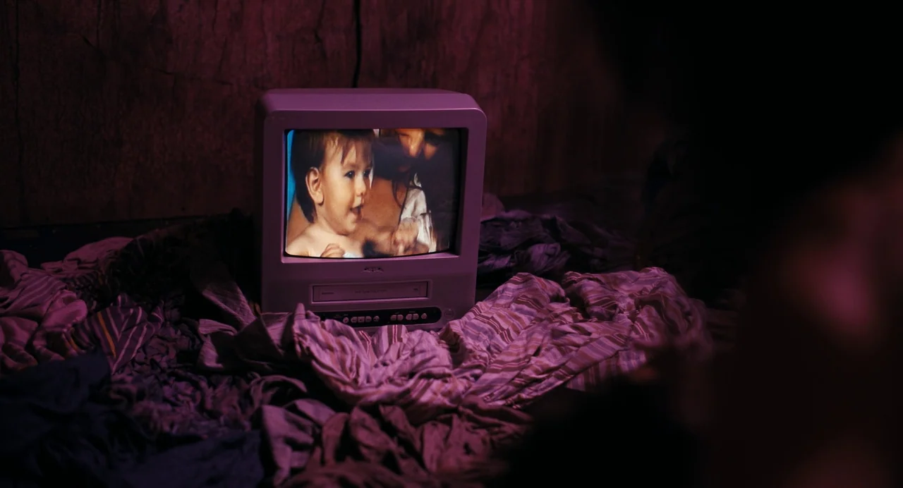 Barbarian (2022) movie still: medium — A small vintage television sits amidst a pile of rumpled striped fabric sheets. The screen depicts a clear…