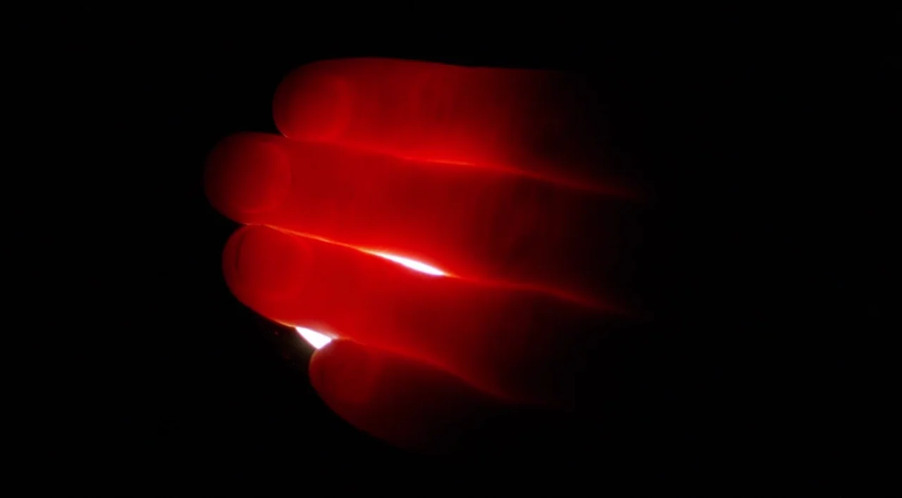 Shallow Grave (1994) movie still: closeup — A dark space contains a single bright light source hidden behind human fingers. The fingers glow a…