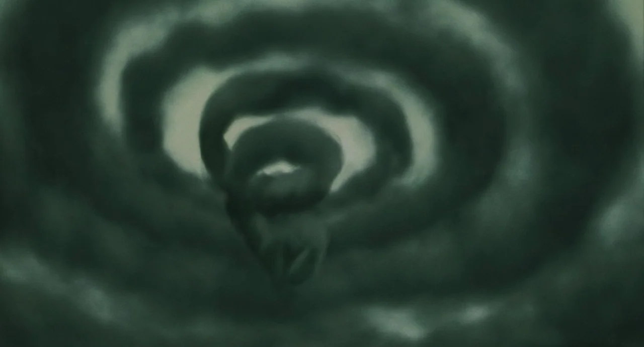 Uzumaki (2000) movie still: wide — Dark, swirling clouds form a circular vortex pattern in a dark night sky. The vapor rotates towards a central…