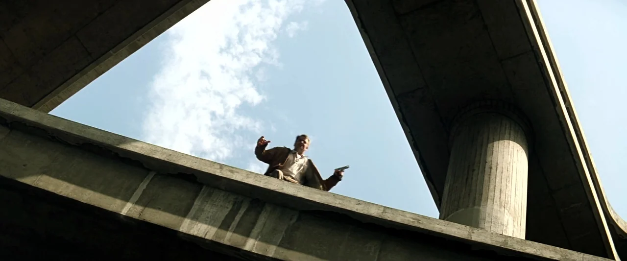 The Last Boy Scout (1991) movie still: wide — A man stands on a concrete highway overpass against a bright, clear sky. He holds a pistol in his hand…