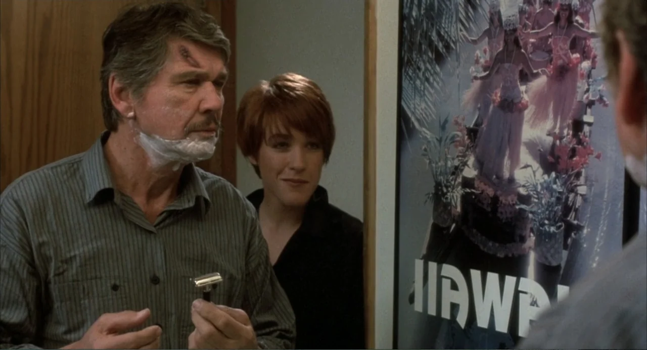 Murphy's Law (2009) movie still: medium — A residential bathroom features a wall mirror displaying a framed travel poster for Hawaii. An older man…