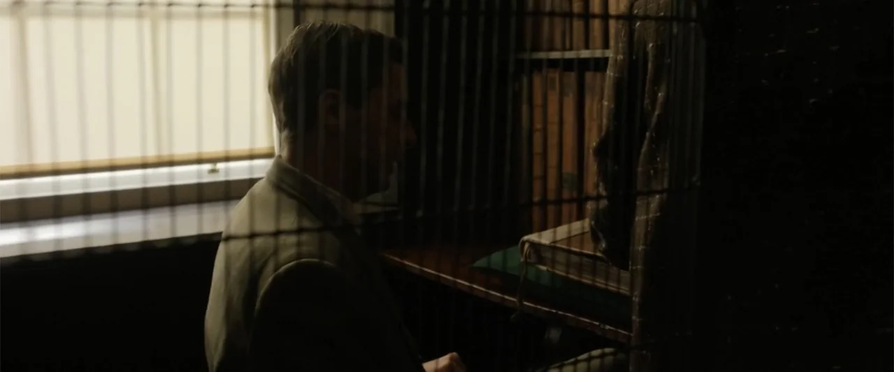 Freud's Last Session (2023) movie still: medium — A dark, cramped archival space features shelves packed with thick, leather-bound books. A man in a…