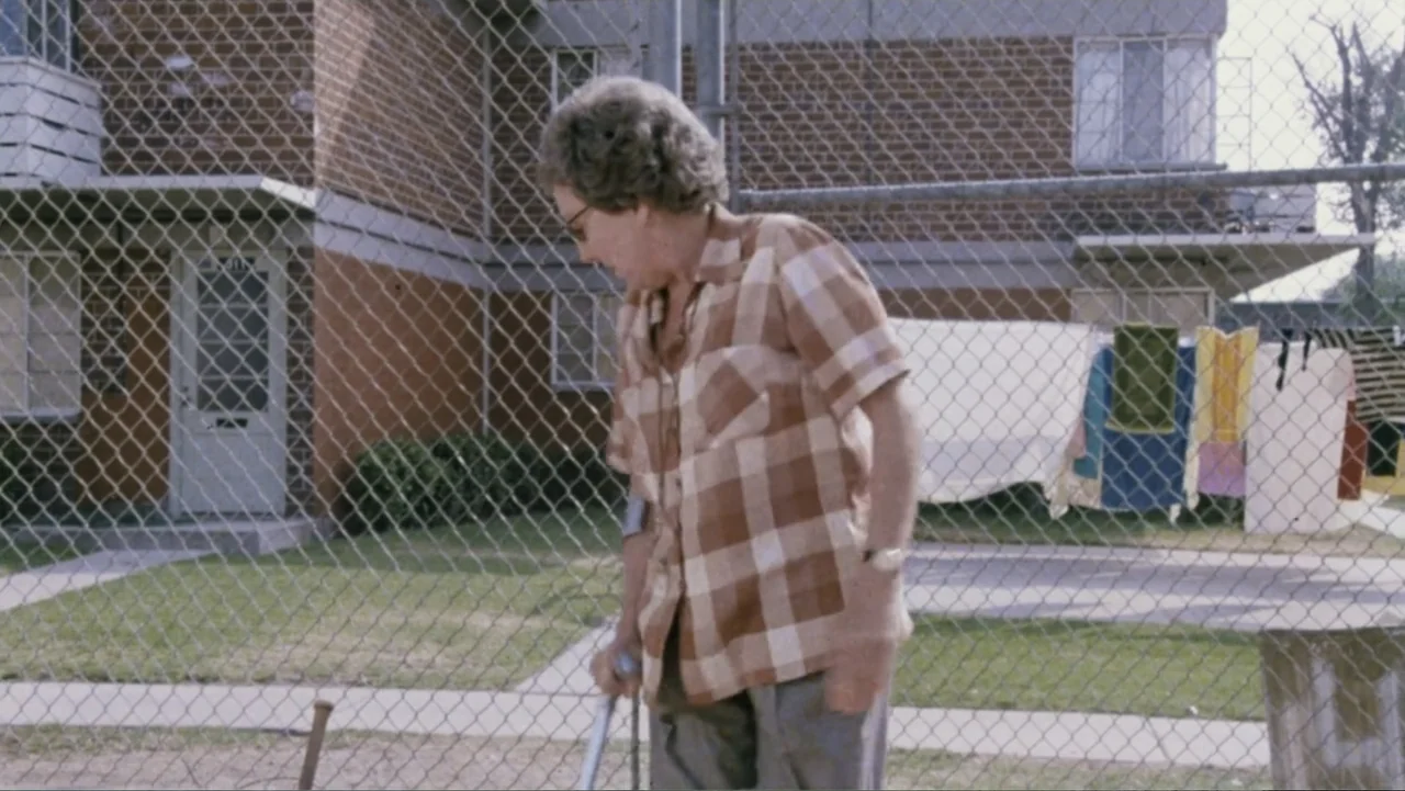 Aunt Mary (1979) movie still: medium — A residential building exterior features a chain-link fence separating the subject from laundry lines. An…