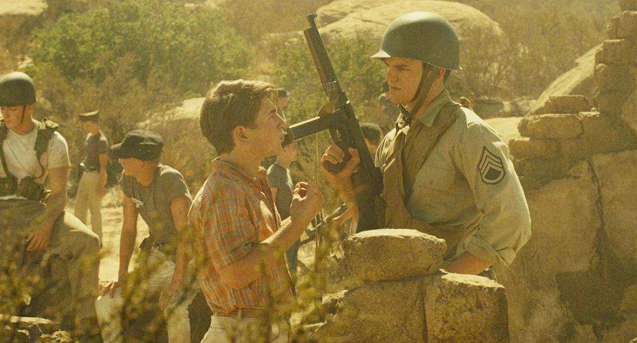 The Fabelmans (2022) movie still: medium — Soldiers in 1950s military uniforms and helmets gather among large rocks in a desert. A young boy in a…