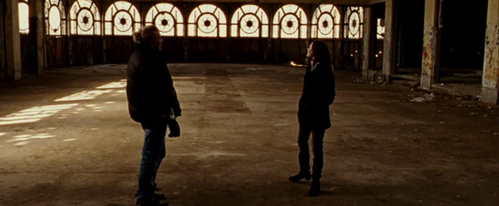 The Wrestler (2008) movie still: wide — A vast, abandoned interior space features numerous arched windows along the back wall. Two individuals stand…
