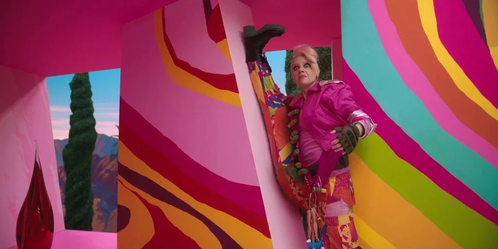 Barbie (2023) movie still: fullbody — An interior space features bright, abstract, multicolored wall panels with large curved patterns. A woman…