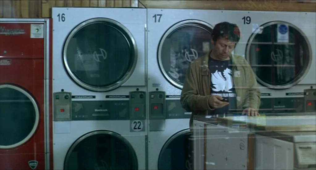 On War (2008) movie still: medium — A row of industrial coin-operated washing machines lines a wood-paneled wall inside a laundromat. A man wearing…