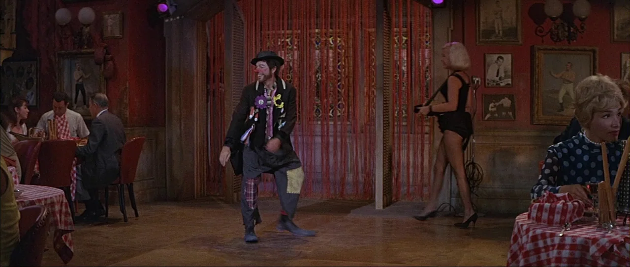 What A Way To Go! (1964) movie still: wide — A restaurant with red walls features framed photographs of boxers and checkered tablecloths. A man…