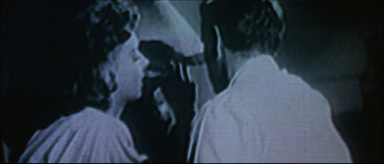 Strange Days (1995) movie still: medium — A dark indoor setting with two figures positioned in a medium close-up. The man stands with his back…