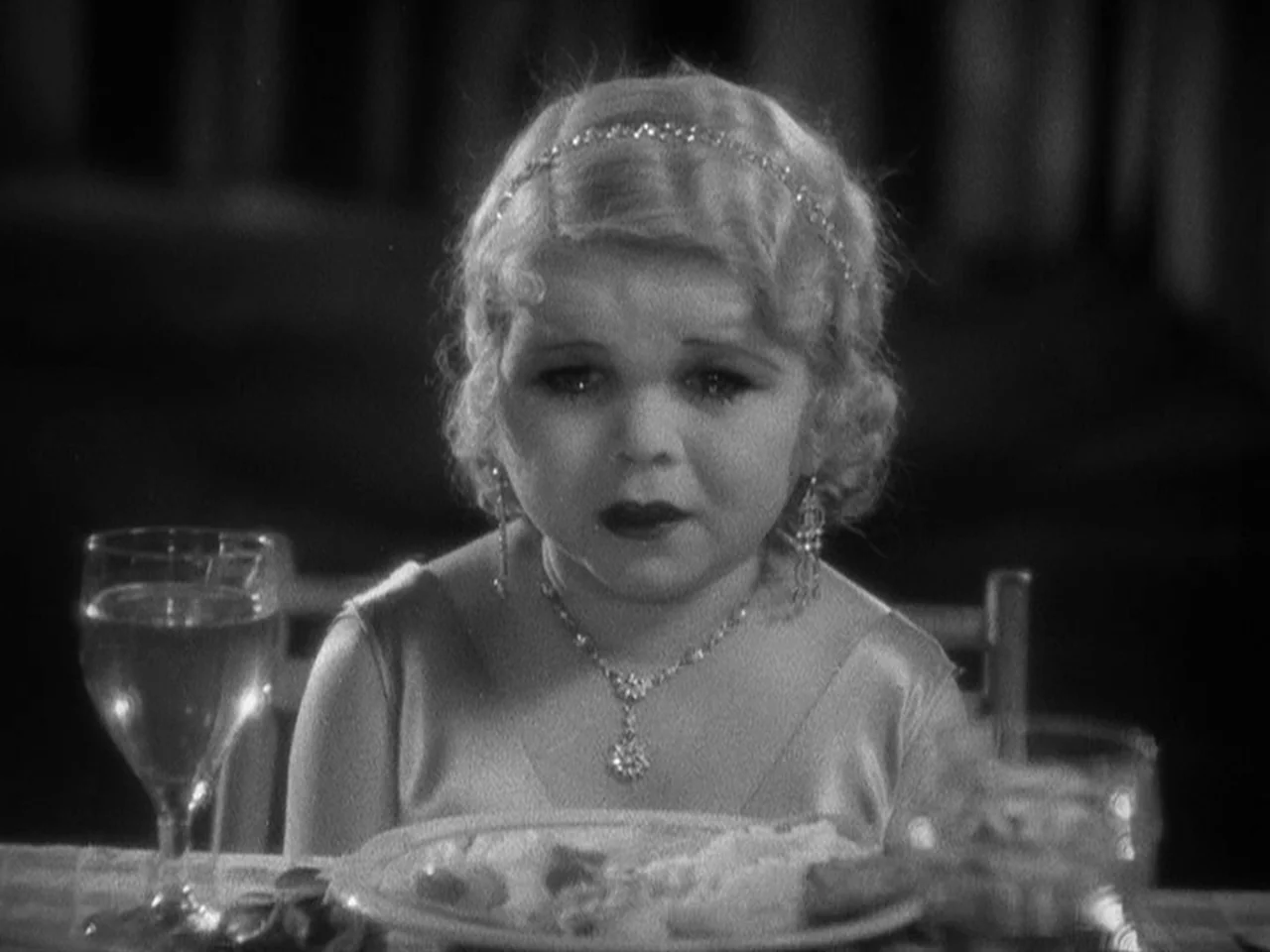 Freaks (1932) movie still: closeup — A 1920s dining table setting features a plate of food and a wine glass. A young woman with finger wave hair and…