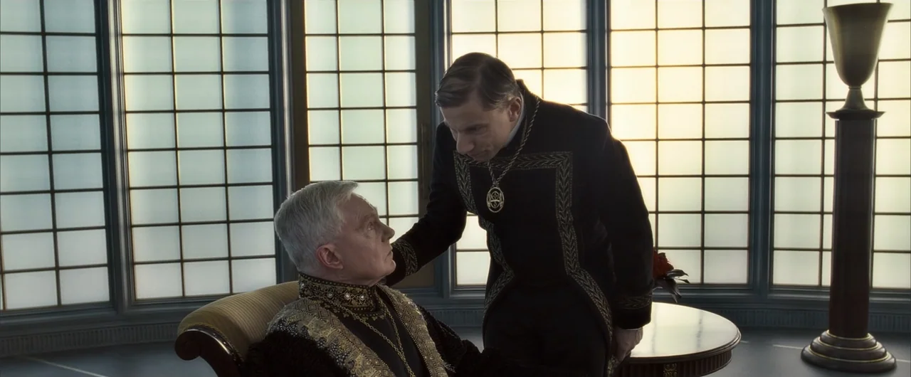 The Golden Compass (2007) movie still: medium — An interior space with large glass windows and ornate historical-style furnishings. An older man…