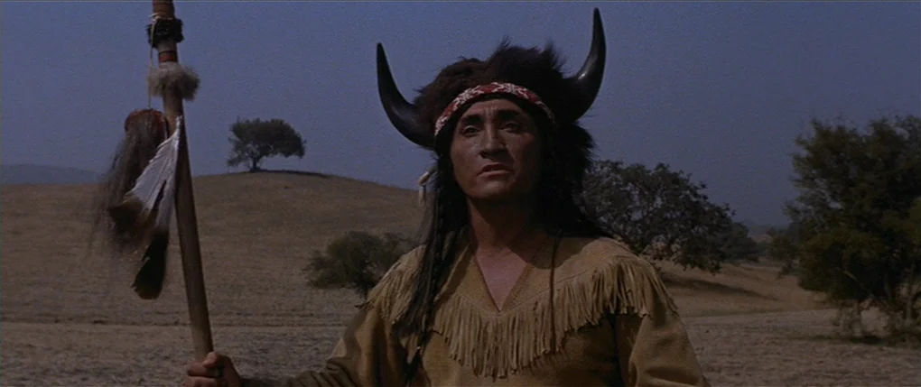 Flaming Star (1960) movie still: medium — An arid, grassy landscape with rolling hills and distant trees under an overcast sky. A man wears a…