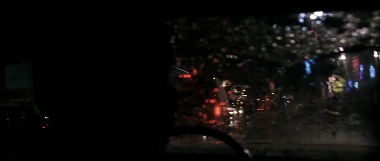 A Man Apart (2003) movie still: medium — A car cabin at night viewed from behind the driver through a rain-covered windshield. The driver sits in…