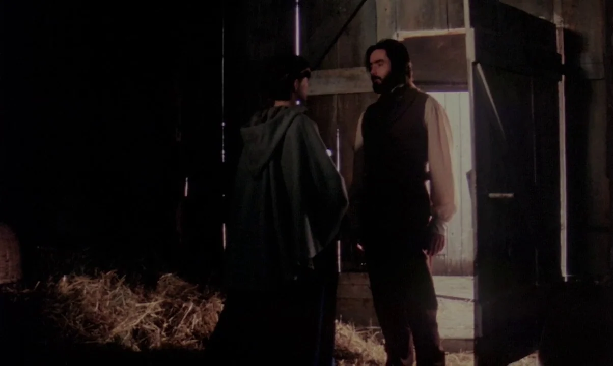 Kamouraska (1973) movie still: fullbody — A dark, wooden barn interior contains scattered hay on the ground. A bearded man speaks to a person in a…