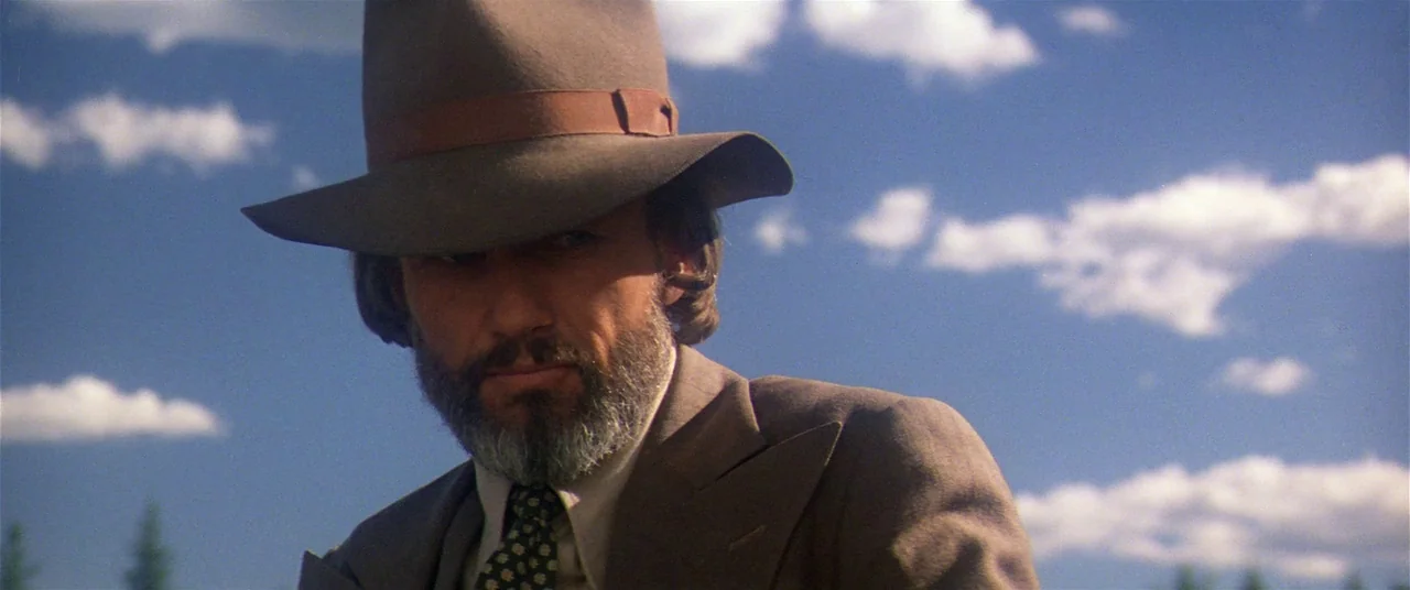 Heaven’s Gate (1980) movie still: closeup — An open landscape with a clear blue sky filled with white clouds. A man wearing a fedora looks directly…