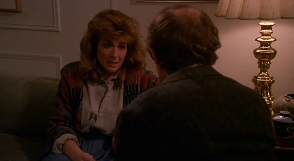 Crimes and Misdemeanors (1989) movie still: medium — A dimly lit room features a woman sitting on a sofa facing an out-of-focus man. A large gold…