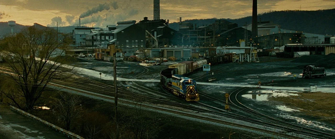 Unstoppable (2010) movie still: establishing — An industrial rail yard features multiple tracks, train cars, and distant smoking factory chimneys. A…