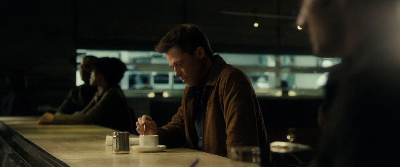 Ad Astra (2019) movie still: medium — A dimly lit modern bar counter at night with blurred figures in the background. A man sits alone at the…