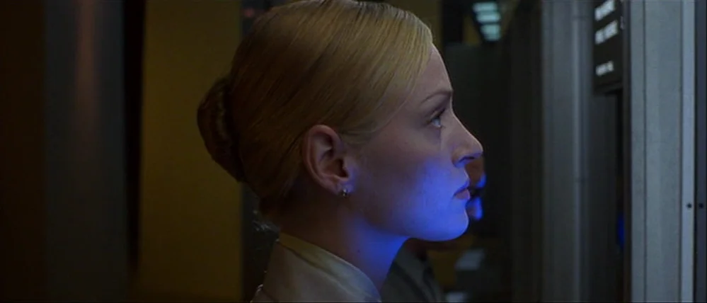 Gattaca (1997) movie still: closeup — A dark, cramped interior space illuminated by a glowing blue digital information screen. A blonde woman in…
