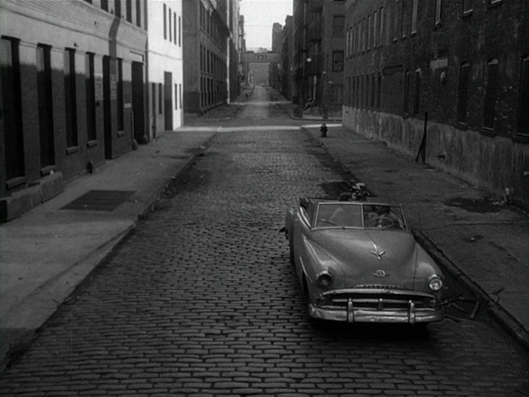 Killer’s Kiss (1955) movie still: wide — An empty cobblestone street is flanked by tall, darkened brick buildings on both sides. A vintage…